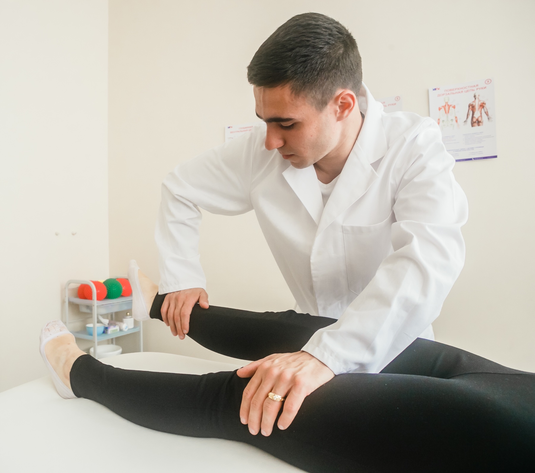 Exame de força muscular nos membros inferiores: examinador aplica resistência à elevação da perna (teste do reto femoral) em adulto jovem em decúbito dorsal.