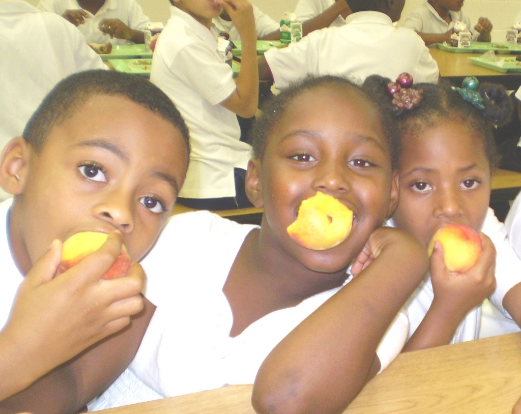 Crianças em idade escolar comendo pêssegos frescos no refeitório, ilustrando alimentação equilibrada na infância.
